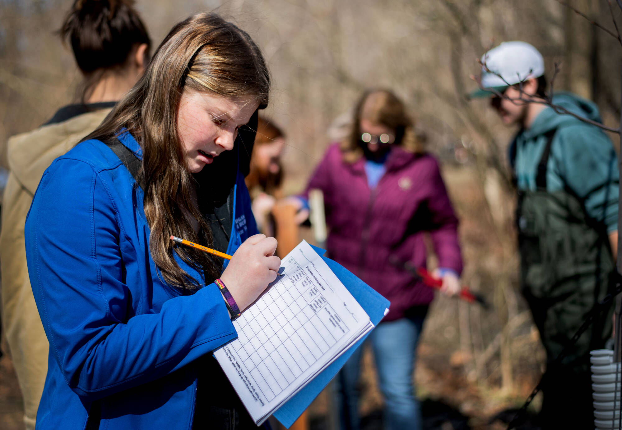 A student fills out a data sheet in the foreground, with another four people out of focus working in the background on data collection